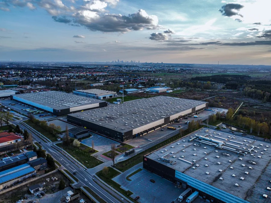Hale przemysłowe z lotu ptaka i panorama miasta na horyzoncie